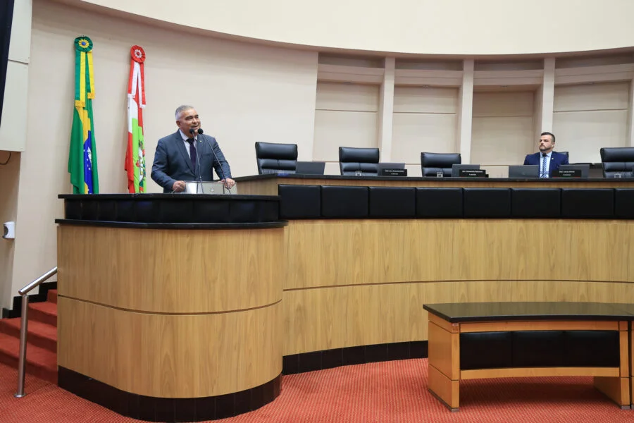 O deputado estadual Sargento Lima (PL) discursa na tribuna da Assembleia Legislativa de Santa Catarina (Alesc) em Florianópolis. Ele fala sobre o direito à legítima defesa das mulheres contra agressões. No fundo, as bandeiras do Brasil e de Santa Catarina estão penduradas na parede.