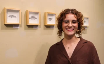Elisa Corrêa abre mostra “Ensaio sobre Coleções” na Unesc A artista visual Elisa Corrêa sorri em frente a quatro quadros com molduras claras contendo desenhos detalhados de mariposas em grafite, durante a abertura da exposição "Ensaio sobre Coleções" no Espaço Cultural Unesc.