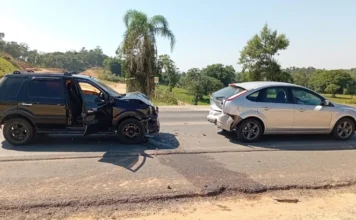 Engavetamento na SC-108 deixa idosa ferida em Cocal do Sul Registro fotográfico de um engavetamento envolvendo dois veículos de passeio na rodovia SC-108, em Cocal do Sul. Um SUV preto apresenta danos na parte dianteira e um hatch prata na traseira, ilustrando a dinâmica da colisão. Marcas de freio e destroços são visíveis na pista de asfalto.