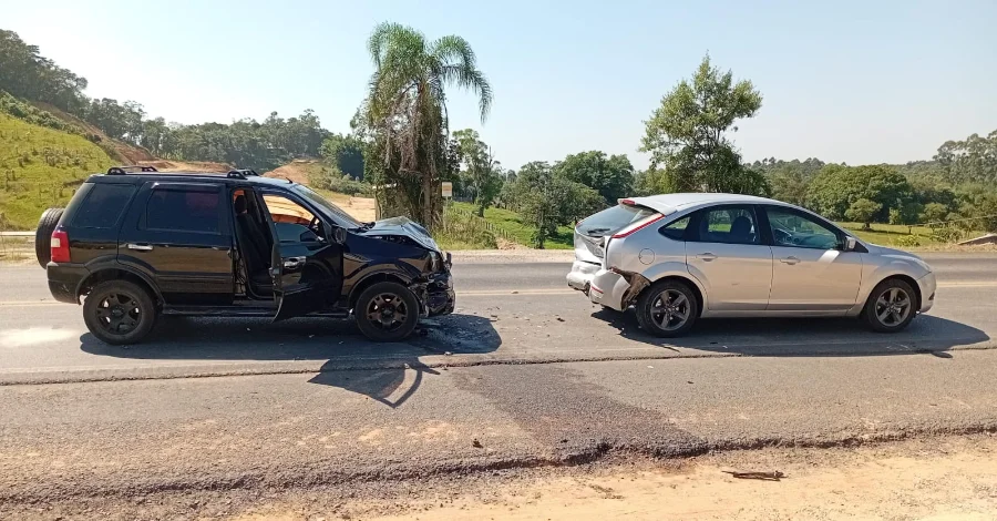 Engavetamento na SC-108 deixa idosa ferida em Cocal do Sul Registro fotográfico de um engavetamento envolvendo dois veículos de passeio na rodovia SC-108, em Cocal do Sul. Um SUV preto apresenta danos na parte dianteira e um hatch prata na traseira, ilustrando a dinâmica da colisão. Marcas de freio e destroços são visíveis na pista de asfalto.