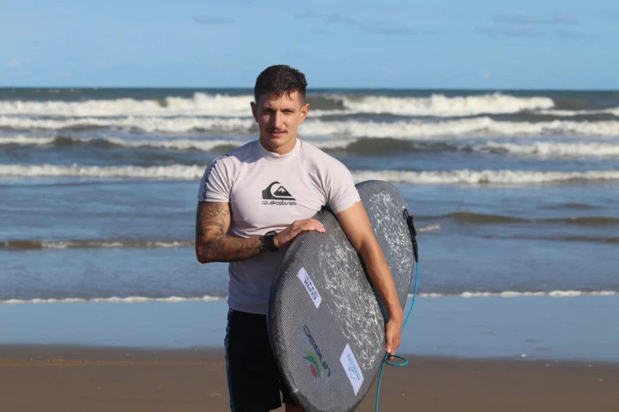 Mateus Salazar, engenheiro e mestre pela Unesc, segurando o protótipo de prancha de surfe inovadora desenvolvida com ciência de materiais. A prancha exibe os logos da Unesc e do Grupo de Pesquisa Cepol.