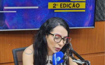 Especialista alerta para riscos cardíacos na menopausa Dra. Araceli Thomaz, cardiologista entrevistada para fazer um alerta sobre a saúde do coração e menopausa, com óculos e tatuagem, falando ao microfone da TV Amorim no estúdio do programa "Jornal Amorim 2ª Edição".
