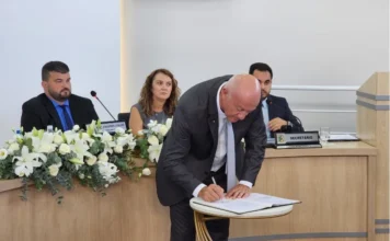 Evandro Scaini renuncia e apresenta balanço de gestão Prefeito Evandro Scaini assinando documento oficial de renúncia sobre mesa na Câmara de Vereadores de Balneário Arroio do Silva.