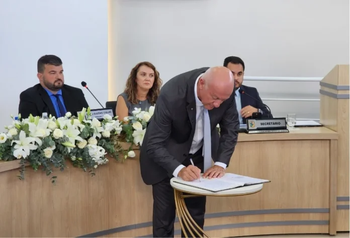 Evandro Scaini renuncia e apresenta balanço de gestão Prefeito Evandro Scaini assinando documento oficial de renúncia sobre mesa na Câmara de Vereadores de Balneário Arroio do Silva.