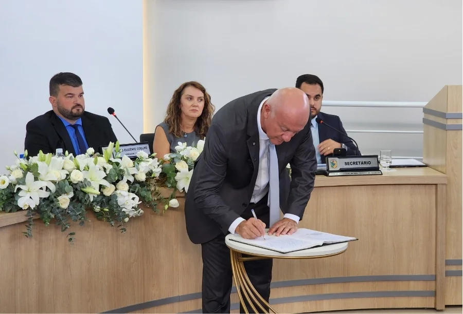 Prefeito Evandro Scaini assinando documento oficial de renúncia sobre mesa na Câmara de Vereadores de Balneário Arroio do Silva.