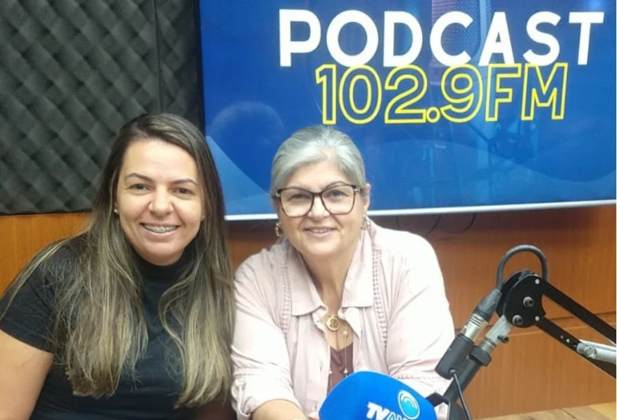 A missionária e pastora Silvia Flôres (à direita) e sua filha, Bruna Flôres (à esquerda), sorriem no estúdio do Podcast 102.9 FM da Rádio Amorim FM durante entrevista de superação.