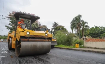 Gabinete Itinerante de Criciúma leva melhorias à Cidade Mineira Rolo compressor amarelo da DTT realiza pavimentação asfáltica em rua da região da Cidade Mineira, Criciúma, durante ação do Gabinete Itinerante. Máquina compacta asfalto novo sobre paralelepípedos com operador visível.