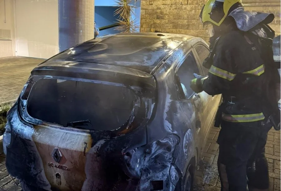 Bombeiro militar do CBMSC trabalha na extinção de incêndio em veículo Renault Kwid carbonizado no Centro de Criciúma. A imagem mostra a parte traseira do carro destruída pelas chamas durante atendimento de ocorrência criminosa na madrugada.