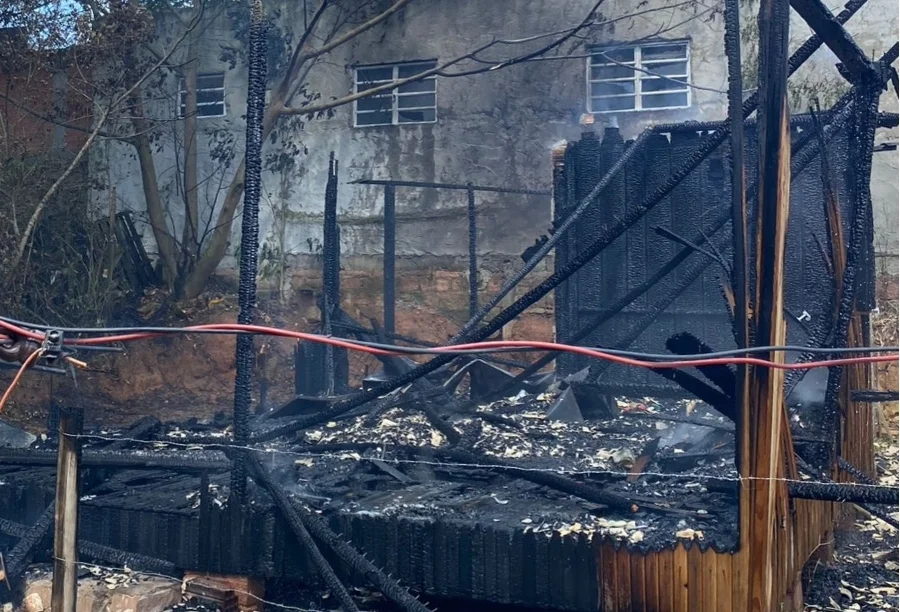 Escombros de residência de madeira totalmente destruída por incêndio no bairro Operária, em Araranguá. A imagem detalha as vigas carbonizadas e os restos da estrutura após o combate às chamas realizado pelo Corpo de Bombeiros (CBMSC).