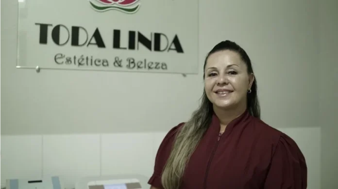 Juro Zero destina R$ 292 milhões para MEIs catarinenses Retrato de Ana Paula Garcia Beumer, beneficiária do crédito Juro Zero, sorrindo em frente ao letreiro de sua clínica 'Toda Linda Estética & Beleza' em Biguaçu, SC.