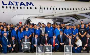 Latam incorpora 24 aviões da Embraer para voos regionais Foto de grupo oficial no hangar MRO em São Carlos, SP, celebrando a entrega dos primeiros jatos Embraer E195-E2 para a Latam. O presidente Lula e o vice-presidente Alckmin estão posicionados na frente com executivos da Latam e da Embraer, rodeados por centenas de funcionários uniformizados. Quatro executivos seguram placas com o design da cauda do avião E2.