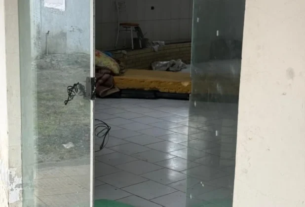 Interior da Capela Mortu&aacute;ria de Sombrio com colch&otilde;es no ch&atilde;o e porta aberta, indicando uso como abrigo.