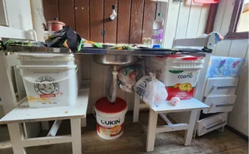 Moradora de Sombrio pede ajuda para enfrentar doenças Pia de cozinha improvisada apoiada sobre cadeiras e baldes plásticos na residência de Dona Neusa, moradora do bairro São Luiz em Sombrio. A imagem detalha a precariedade das instalações e a necessidade urgente de doação de um balcão de pia e móveis básicos.