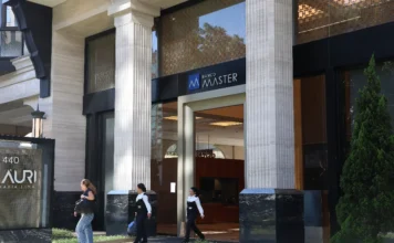 PF identifica R$ 2,2 bi ocultos por Vorcaro na Reag Fotografia da fachada do Banco Master, localizado na Avenida Faria Lima, em São Paulo. A imagem mostra a entrada principal do edifício, caracterizada por grandes colunas de pedra em estilo clássico e portas de vidro. No topo da entrada, vê-se o logotipo azul e a inscrição "Banco Master". No lado esquerdo, um totem indica o número 440 da via. Três mulheres caminham pela calçada em frente ao prédio, vestindo uniformes escuros e camisas brancas, sob a luz do dia.