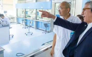 Padilha busca tecnologia na China para modernizar o SUS Uma visita oficial a um moderno laboratório de pesquisa de biotecnologia. Um dignitário ocidental em terno escuro ouve atentamente enquanto um cientista local em jaleco branco aponta para equipamentos médicos avançados. Cena de cooperação internacional em tecnologia médica, mostrando intercâmbio científico e desenvolvimento de parcerias.
