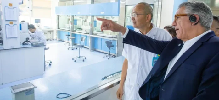 Padilha busca tecnologia na China para modernizar o SUS Uma visita oficial a um moderno laboratório de pesquisa de biotecnologia. Um dignitário ocidental em terno escuro ouve atentamente enquanto um cientista local em jaleco branco aponta para equipamentos médicos avançados. Cena de cooperação internacional em tecnologia médica, mostrando intercâmbio científico e desenvolvimento de parcerias.