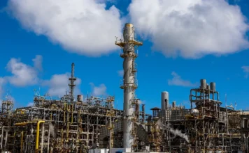 Petrobras eleva preço do diesel em R$ 0,38 Vista detalhada da infraestrutura de uma refinaria de petróleo da Petrobras, exibindo torres de processamento, chaminés e complexa rede de tubulações industriais sob um céu azul com nuvens. Imagem focada na produção de combustíveis e refino de diesel no Brasil.