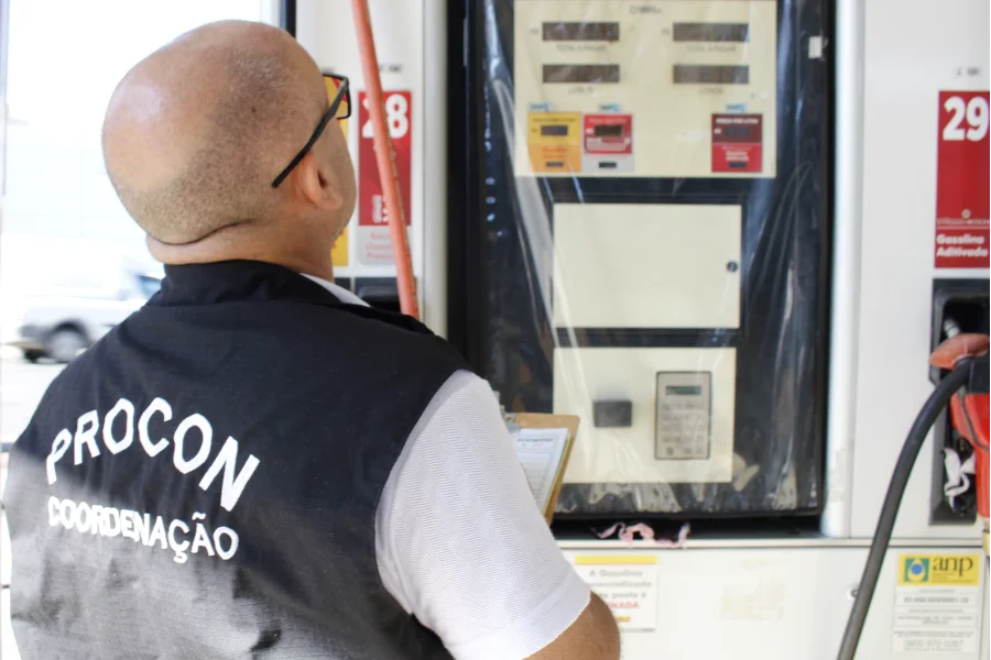 Agente do Procon Criciúma com colete de coordenação inspeciona bomba de combustível durante fiscalização de preços em posto de gasolina.