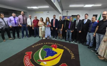 Professora recebe medalha por salvar aluno em Sombrio Professora Juliana Martins Vargas segura a Medalha Padre João Reitz ao lado de vereadores e familiares no plenário da Câmara Municipal de Sombrio durante sessão de homenagem por ato de bravura.