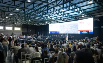 Próxima Alesc Itinerante será em Araranguá em maio Grande público assiste a sessão da Alesc Itinerante em Curitibanos, Santa Catarina, com deputado Julio Garcia discursando no palco. A foto mostra cadeiras brancas e um grande painel de LED ao fundo com a marca do programa.
