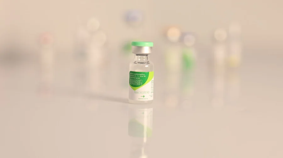 Frasco da vacina contra o HPV (Papilomavírus Humano) em destaque sobre superfície clara e refletora, simbolizando a imunização e prevenção do câncer de colo do útero em Santa Catarina.