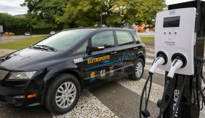 SC cria grupo de trabalho para impulsionar carros elétricos Carro elétrico preto da Celesc estacionado ao lado de estação de carregamento WEG WEMOB Parking em eletroposto público de Santa Catarina. Imagem mostra infraestrutura para eletromobilidade com logos da Aneel e Celesc.