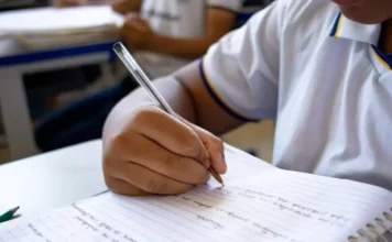 SC investe R$ 94,4 milhões em segurança nas escolas Close de mão de aluno escrevendo com caneta em caderno durante aula em escola da rede estadual de Santa Catarina, representando o cotidiano escolar.