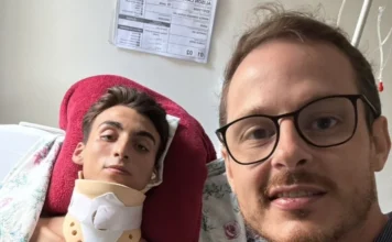 SC terá primeira aplicação de polilaminina em Sombrio Uma fotografia do tipo selfie, tirada em um quarto de hospital, mostra em primeiro plano, à direita, o Dr. Ângelo Formentin Neto, médico residente de anestesiologia e coordenador do Pronto Socorro, de óculos e sorrindo para a câmera. À esquerda, deitado na cama e apoiado por um travesseiro vermelho, está o paciente Alison Carvalho Saldívia, de 19 anos, que usa um colar cervical rígido. Alison olha diretamente para a câmera. Ao fundo, na parede branca, estão fixadas tabelas e prontuários médicos. A imagem ilustra o médico que viabilizou o tratamento experimental ao lado do paciente que será o primeiro em Santa Catarina a receber a aplicação de polilaminina.