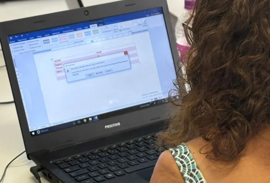 Santa Rosa do Sul abre inscrições para curso de informática Participante de curso de informática básica da prefeitura de Santa Rosa do Sul, com laptop Positivo exibindo interface de processador de texto e uma caixa de diálogo de erro.