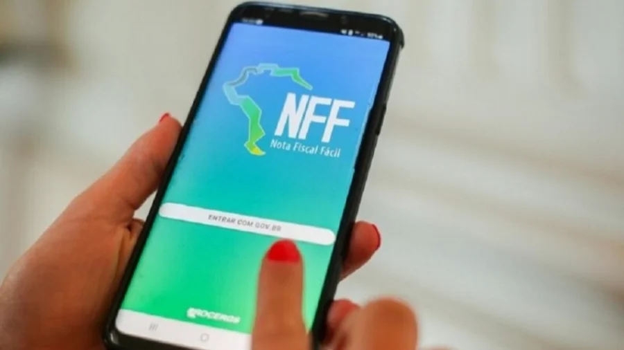 Mãos de uma mulher segurando um smartphone que exibe a tela de login do aplicativo Nota Fiscal Fácil (NFF) para produtores rurais, com o logotipo da Procergs e o botão 