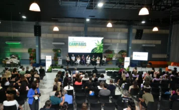 Simpósio em Criciúma debate avanços da cannabis medicinal Público acompanha painel de especialistas durante o 1º Simpósio de Cannabis Medicinal no Centro de Inovação Criciúma (CRIO). A imagem mostra o auditório lotado e palestrantes no palco sob um telão com a identidade visual do evento da Unesc.