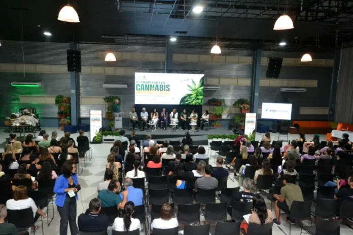 Simpósio em Criciúma debate avanços da cannabis medicinal Público acompanha painel de especialistas durante o 1º Simpósio de Cannabis Medicinal no Centro de Inovação Criciúma (CRIO). A imagem mostra o auditório lotado e palestrantes no palco sob um telão com a identidade visual do evento da Unesc.