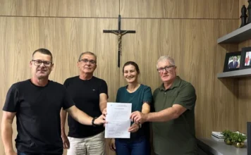 Timbé do Sul assina ordem para obra de farmácia pública Prefeito Vilmar Maffiolette e a Secretária de Saúde de Timbé do Sul, Sabrina Moro Pizzolo, ladeados por outras autoridades municipais, seguram o documento de ordem de serviço assinado para o início das obras da nova farmácia pública municipal, anexa ao Posto Central. Foto posada em escritório de prefeitura.