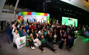 Unesc abre inscrições para a Cofafe 2026 em Brusque Delegação campeã da Unesc em celebração com o troféu geral da Cofafe (Acafe) no palco. Professores e funcionários seguram medalhas e uma bandeira da instituição, diante de um banner colorido e telão de LED.