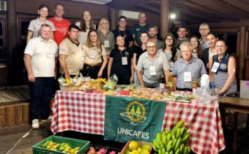 Unesc capacita dirigentes de cooperativas em Jaguaruna Grupo de participantes do curso de formação para dirigentes cooperativistas da Unesc reunidos atrás de uma mesa com produtos da agricultura familiar, como bananas e pitayas, em Jaguaruna. No centro, destaca-se a bandeira da Unicafes.