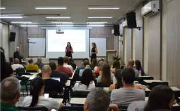 Unesc debate excelência na pós-graduação em Aula Magna Foto de auditório na Unesc com público assistindo a uma apresentação. No palco, a coordenadora da Capes, Verônica Calado, fala ao microfone. No telão, informações sobre a Aula Magna do PPGCEM (Ciência e Engenharia de Materiais) Unesc.