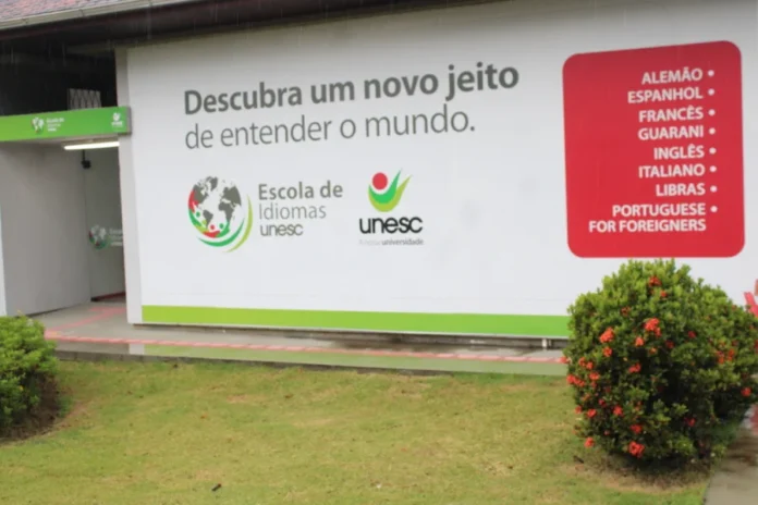 Unesc sedia evento inédito sobre ensino de idiomas Fachada da Escola de Idiomas da Unesc em Criciúma com painel exibindo a lista de cursos oferecidos, local que sedia o evento de formação para professores BRAZ-TESOL Santa Catarina.