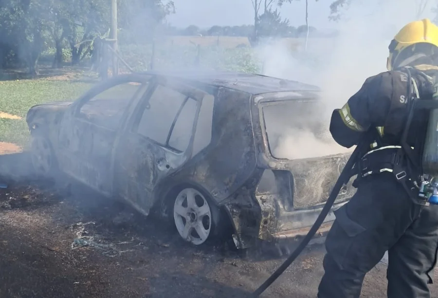 Bombeiro militar combatendo incêndio em automóvel Volkswagen Golf no bairro Rio dos Anjos, em Araranguá. O veículo está tomado por fumaça e apresenta danos severos na estrutura após ser atingido pelas chamas.