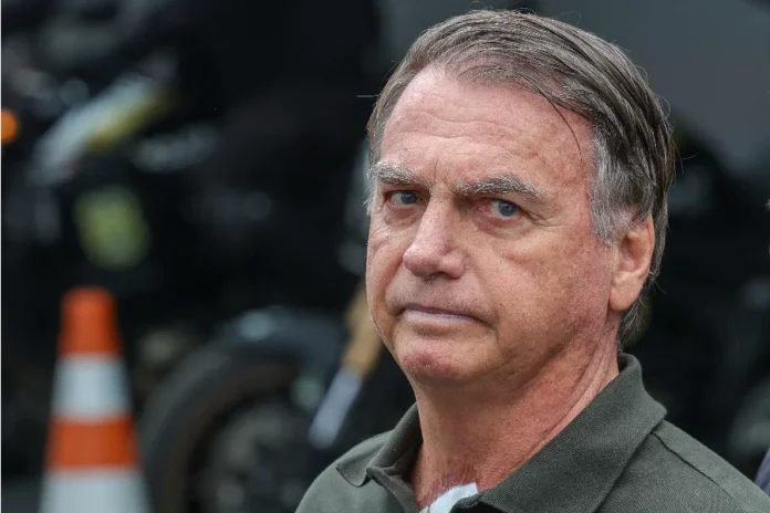 jair-bolsonaro-expressao-seria-agencia-brasil Jair Bolsonaro em primeiro plano com expressão séria e olhar fixo; ao fundo, motocicletas e sinalização de trânsito desfocadas durante evento público.