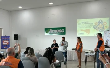 AMESC debate segurança escolar e prevenção de riscos em SC Representantes da AMESC e Defesa Civil de Santa Catarina em palestra sobre segurança escolar e o plano Plancon Edu-Multirriscos, com projeção e público presente em auditório.