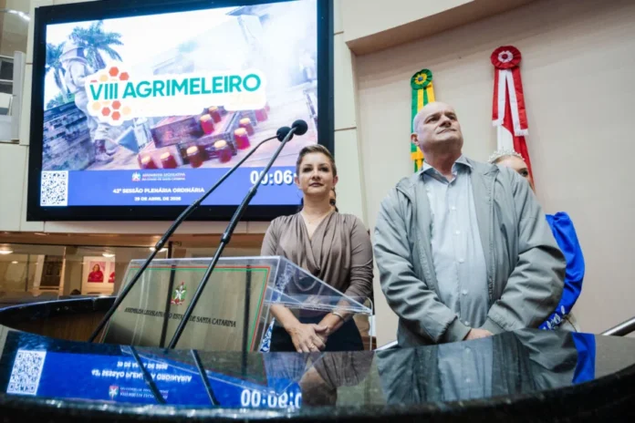 Agrimeleiro Comitiva convida Alesc para evento em maio Prefeito de Meleiro, Anderson Scarduelli, e Jovana Peterle na tribuna da Assembleia Legislativa de Santa Catarina (Alesc) apresentando o cartaz digital da 8ª Agrimeleiro no telão ao fundo para divulgação do evento agrícola.