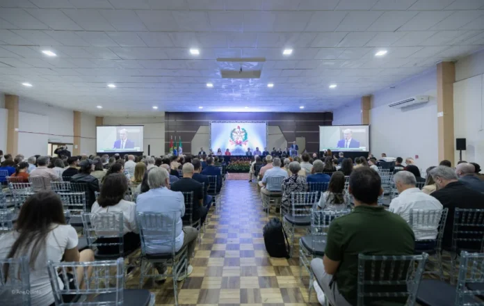 Alesc celebra 120 anos da Escola Catulo em Sombrio Visão ampla do auditório lotado do Sombrio Tênis Clube durante a sessão solene da Alesc que celebrou os 120 anos da Escola Catulo da Paixão Cearense. O palco principal tem o brasão da Assembleia Legislativa de Santa Catarina e telas de projeção mostrando o palestrante. O público está sentado em cadeiras transparentes.