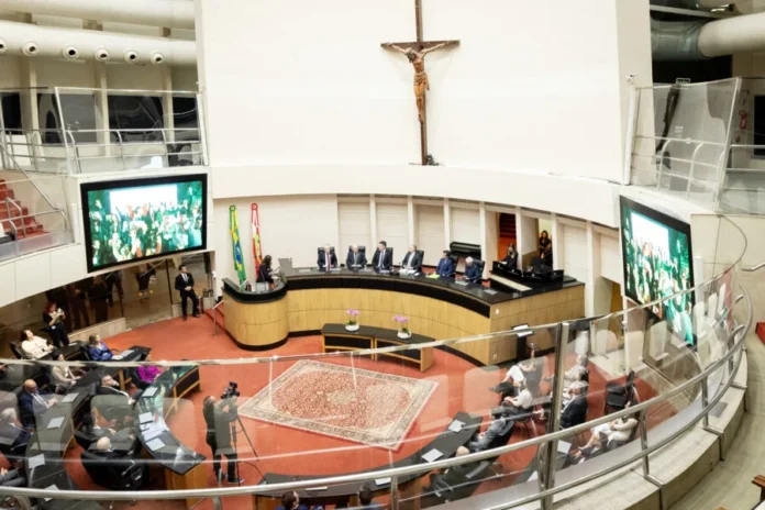 Alesc homenageia 40 anos da Acate em sessão especial Plenário da Assembleia Legislativa de Santa Catarina (Alesc) durante sessão especial em homenagem aos 40 anos da ACATE, em Florianópolis. A imagem mostra a mesa diretiva com autoridades, telas laterais exibindo os participantes e o público presente no evento de tecnologia e inovação.