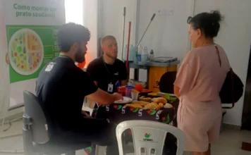 Alunos da Unesc realizam avaliação nutricional em Criciúma Acadêmicos de Nutrição da Unesc realizam ação de educação alimentar na UBS Centro de Criciúma, orientando paciente sobre como montar um prato saudável com modelos de alimentos sobre a mesa.