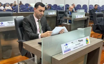 Araranguá aprova criação dos Jogos da Terceira Idade O vereador Márcio Mano sentado em sua bancada na Câmara Municipal de Araranguá, lendo o documento do anteprojeto de lei dos Jogos da Terceira Idade durante sessão ordinária. Ao fundo, outros vereadores e a galeria do plenário.