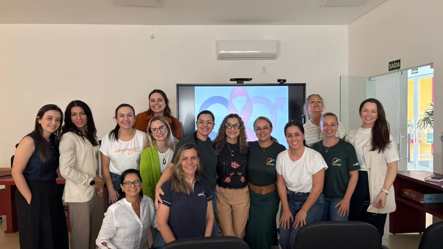 Grupo de enfermeiras da rede municipal de saúde de Araranguá reunidas em sala de treinamento durante capacitação técnica sobre tuberculose e testes rápidos de HIV e sífilis. Ao fundo, uma tela exibe símbolos de conscientização em saúde.