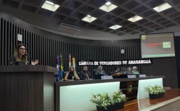 Araranguá discute estratégias de combate ao feminicídio Delegada Eliane Chaves discursa na tribuna da Câmara de Vereadores de Araranguá sobre o aumento dos casos de feminicídio em Santa Catarina. Ao fundo, mesa diretora da casa e tela de projeção com o alerta "Feminicídios em alta".