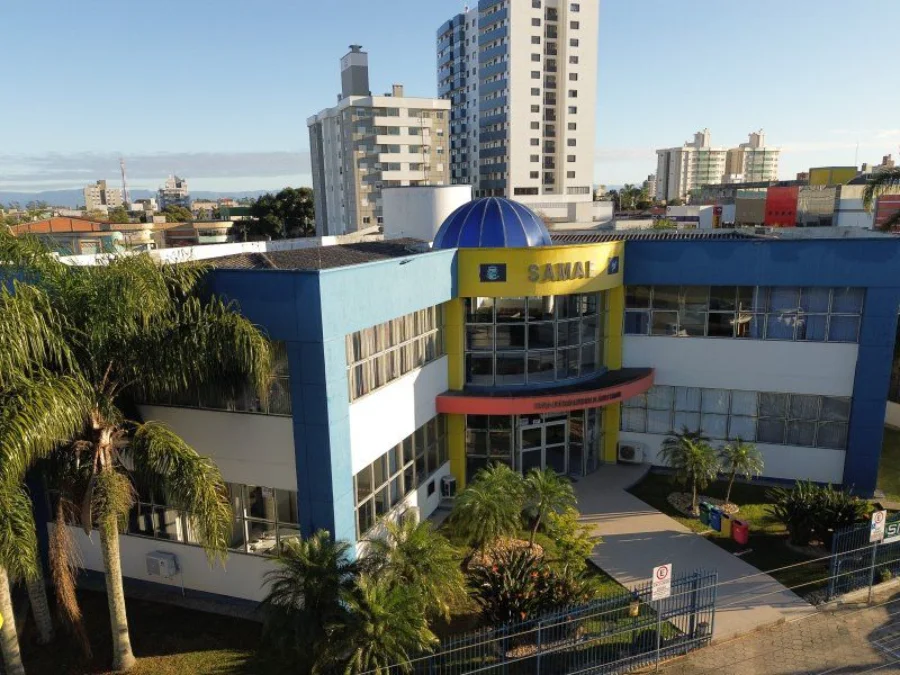 Fachada frontal da sede do SAMAE Araranguá em dia ensolarado. O prédio do Serviço Autônomo Municipal de Água e Esgoto exibe cores azul e amarelo com arquitetura moderna, simbolizando a infraestrutura de saneamento básico e os investimentos hídricos nos 146 anos do município.