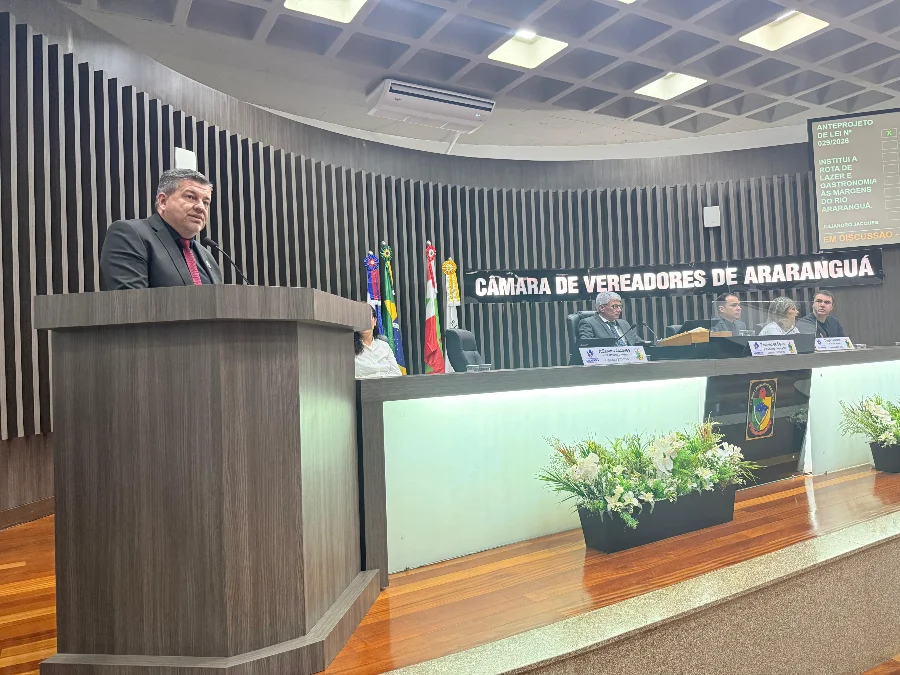 Araranguá planeja rota gastronômica às margens do rio Vereador Juliandro Jacques discursa na tribuna da Câmara de Vereadores de Araranguá sobre a criação da Rota de Lazer e Gastronomia às margens do Rio Araranguá. Ao fundo, painel eletrônico detalha o Anteprojeto de Lei 029/2026 durante a sessão ordinária.