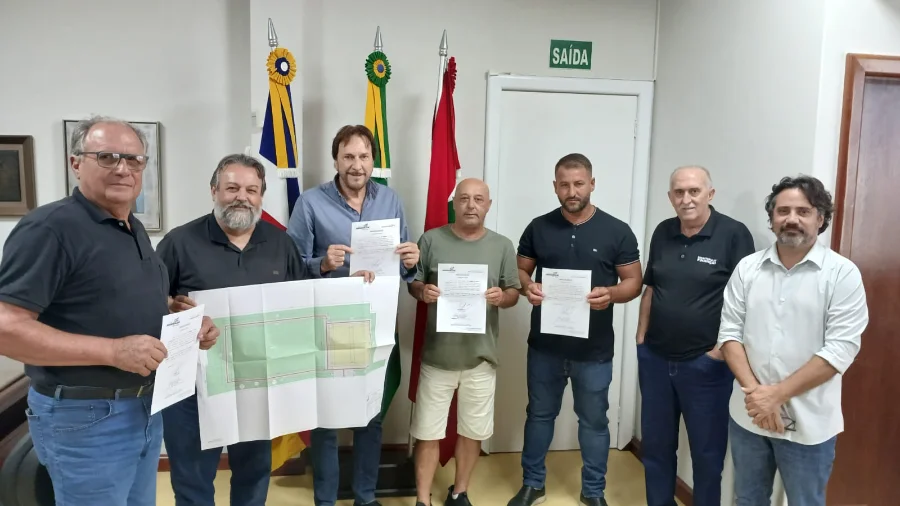 Prefeito Cesar Cesa e autoridades de Araranguá seguram a planta do projeto e a ordem de serviço assinada para a construção da nova praça no bairro Coloninha. A imagem destaca o ato oficial de investimento em lazer e infraestrutura urbana no município.